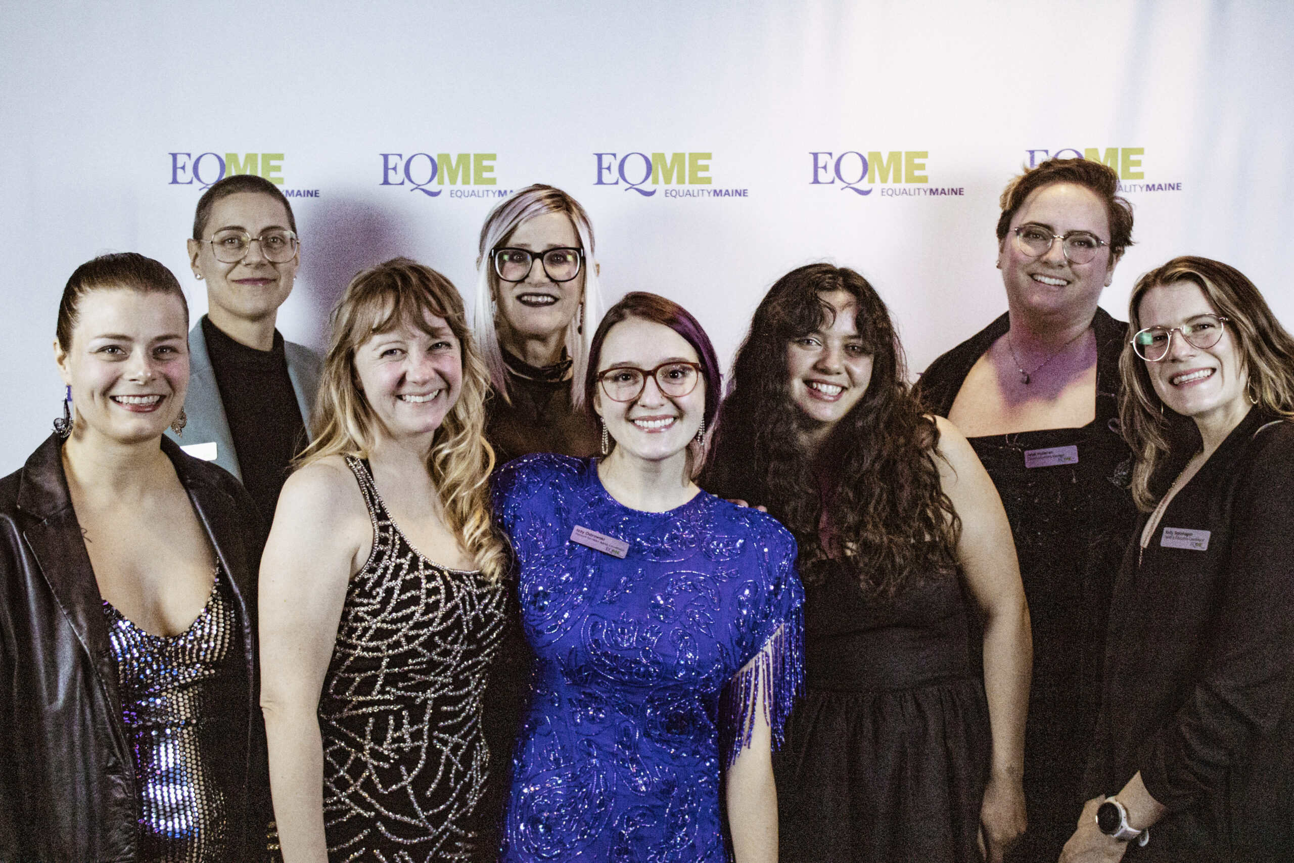 A group of eight people smiling with an Equality Maine photo backdrop behind them.